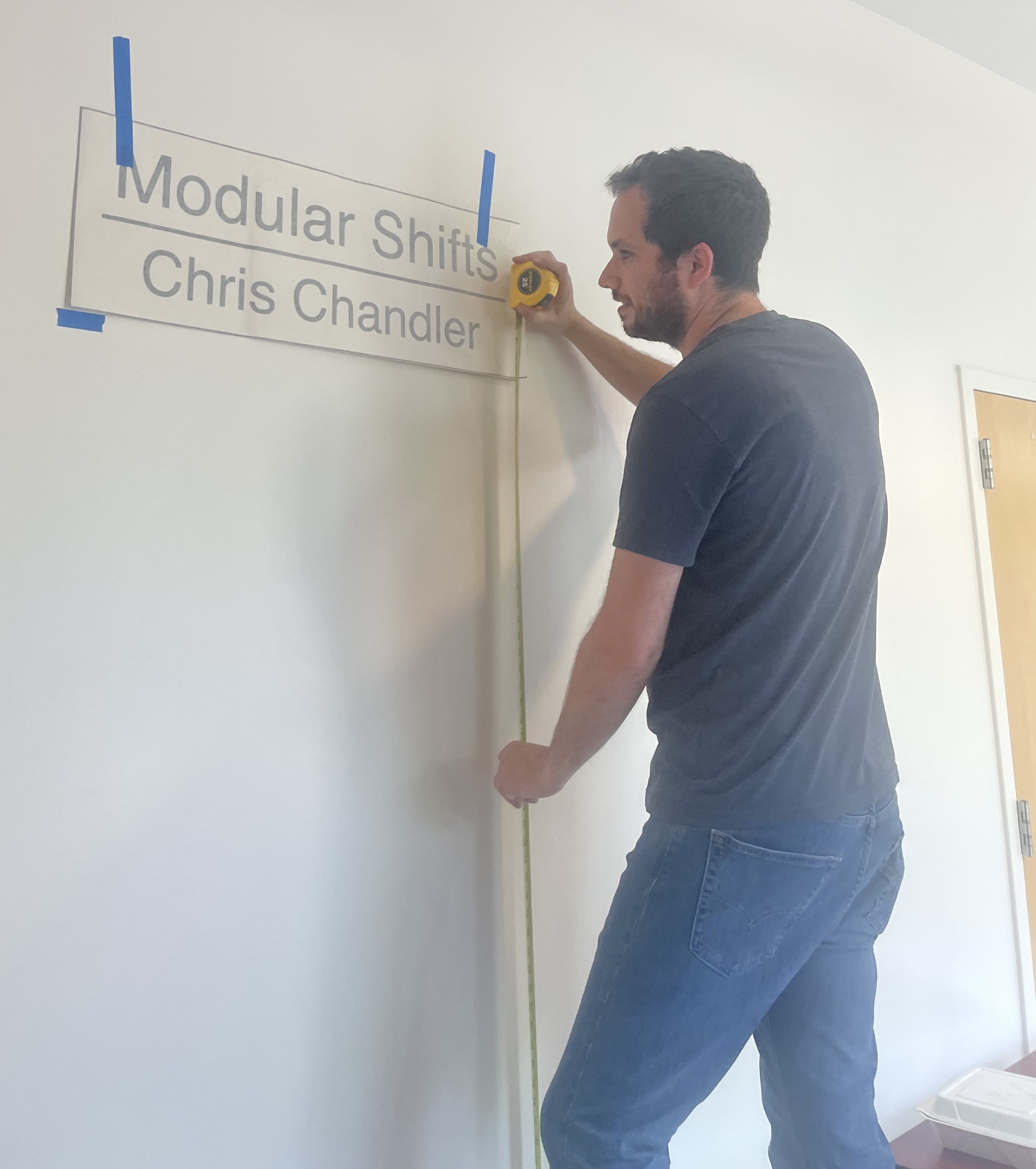 Gallery technician Noah Matteucci installs the exhibition title for Modular Shifts by Chris Chandler. (Photo courtesy of Noah Matteucci)