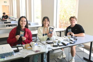 A photo showing Vice President Alicia Salazar, Treasurer Tiffany Vu, and President Ashton Wagner, smiling while making care kits.