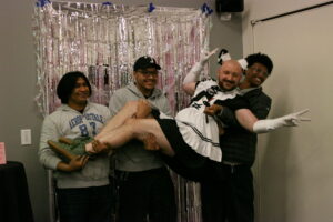 Photo shows 3 students posing with on the student maids, in this case the 3 students are lifting the maid. Photo taken by Will Legg.
